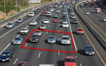 An aerial photograph of dense traffic on a multi-lane highway, with a red rectangle drawn around one car and the three vehicles immediately surrounding it