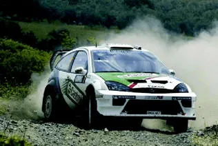 A rally car at speed on a gravel road, sliding through a bend with dust streaming from its rear wheels
