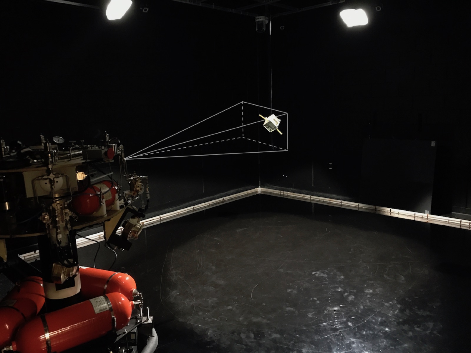 The ASTROS test arena: the platform with red high-pressure tanks in the foreground, a suspended CubeSat target, and an overlaid camera field-of-view cone